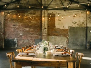 Stijlvol gedekte evenementtafel met elegant glaswerk en bloemstukken in industriële bakstenen zaal met sfeervolle Edison-peertjes.