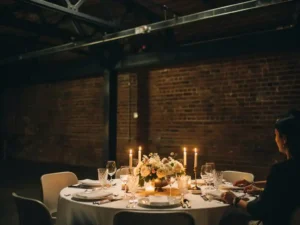 Intiem dinertafel met kaarsen en bloemen in een industriële ruimte met bakstenen muren en stalen balken.